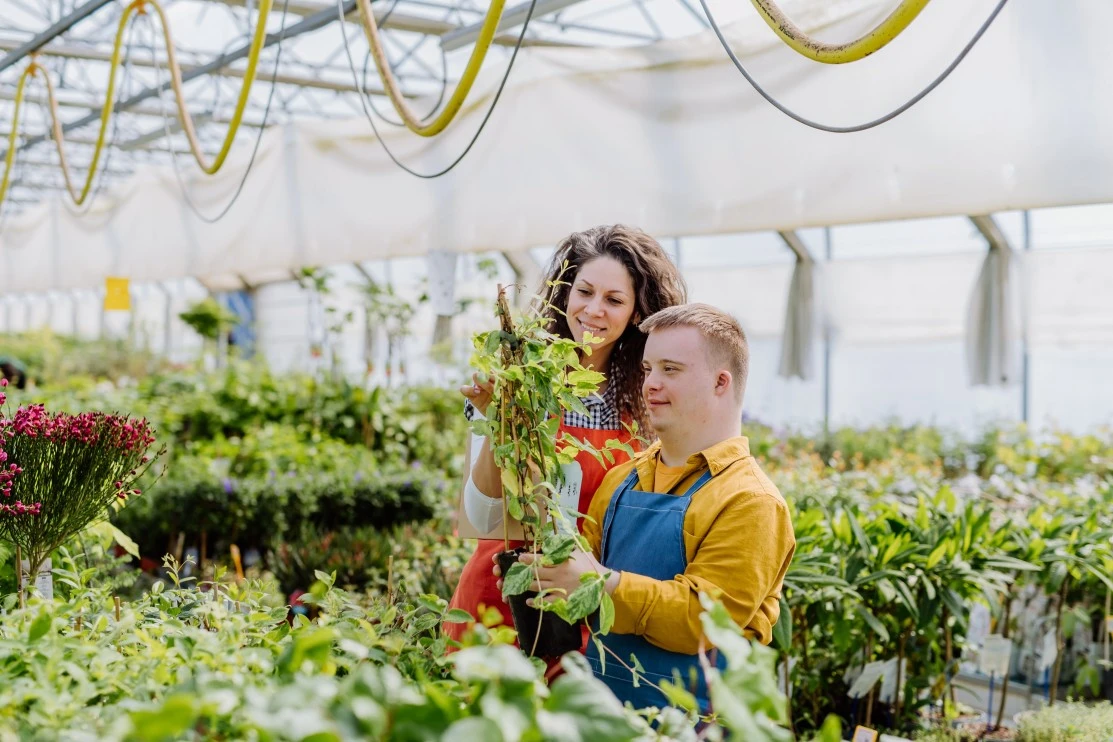 Happy disabled man with down syndrome with support worker in greenhouse